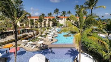 A resort pool area with multiple swimming pools, palm trees, and lounge chairs.