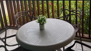 Un balcon avec une table ronde et des chaises, donnant sur un espace piscine agrémenté de parasols et de palmiers.