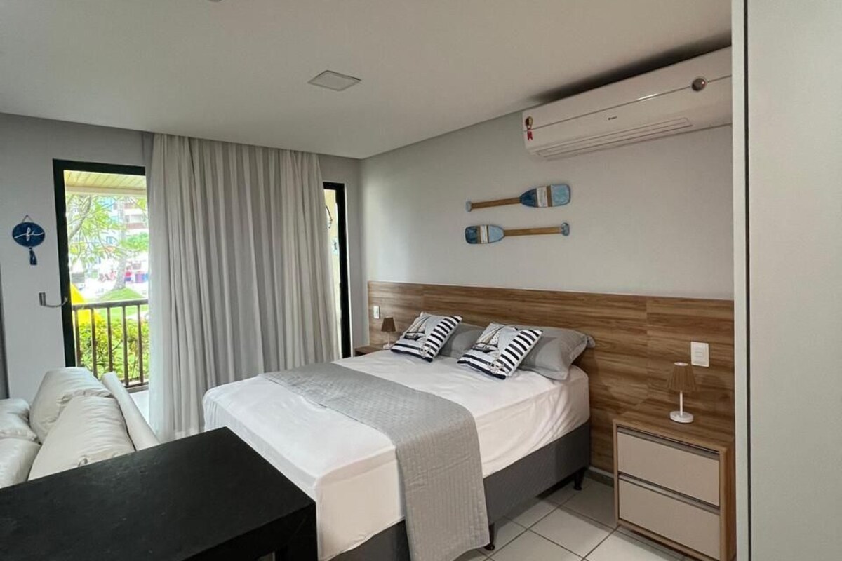 A modern bedroom with a bed, bedside tables, a desk, and a view of the outdoors.