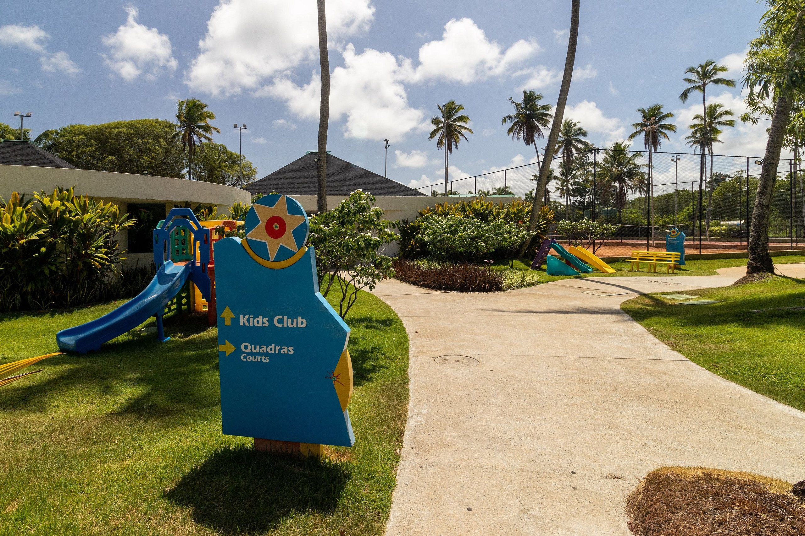 Een speelplaats met een glijbaan en een bord waarop 'Kids Club' en 'Quadras Courts' staat.