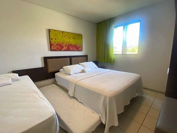 A hotel room with two beds, a headboard, a painting on the wall, and a window with curtains.