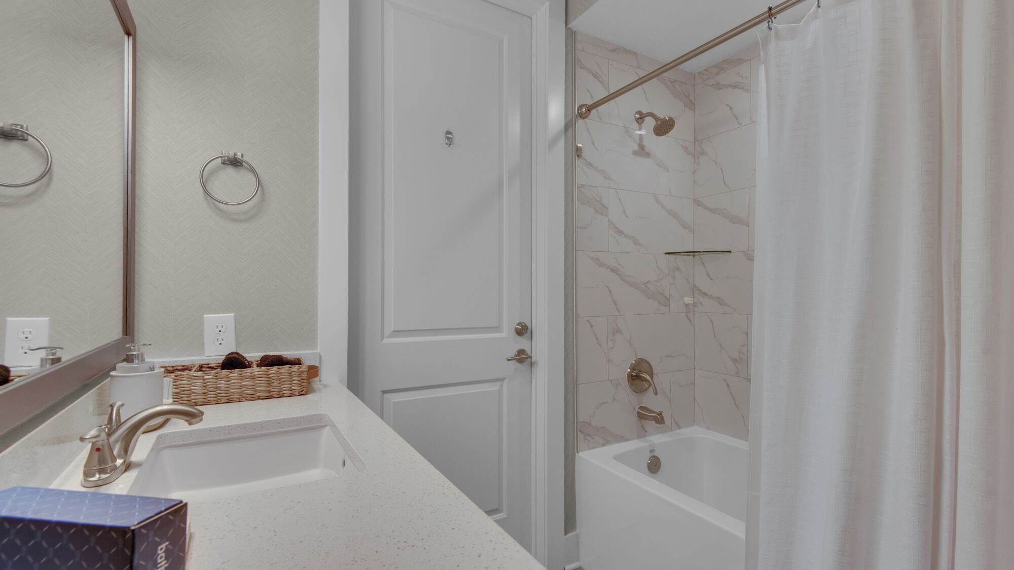 A bathroom with a white sink, a mirror, a shower with a glass door, and a marble-tiled shower area.