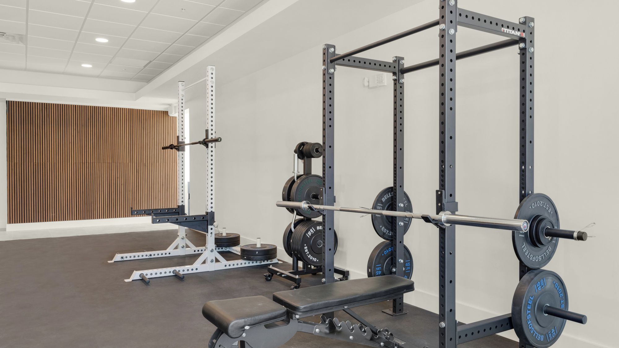 A gym with weightlifting equipment, a bench, and a wooden panel wall.