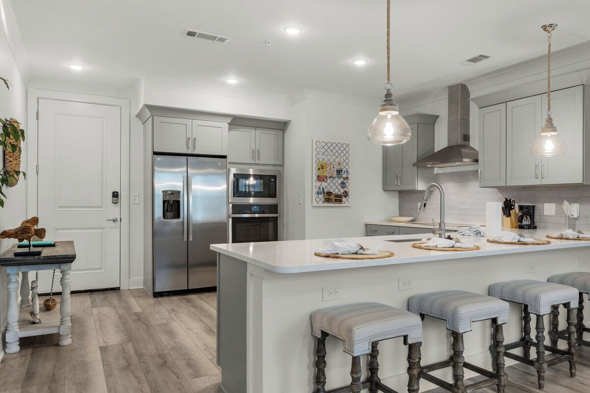 A modern kitchen with stainless steel appliances, a central island with bar stools, and pendant lighting.