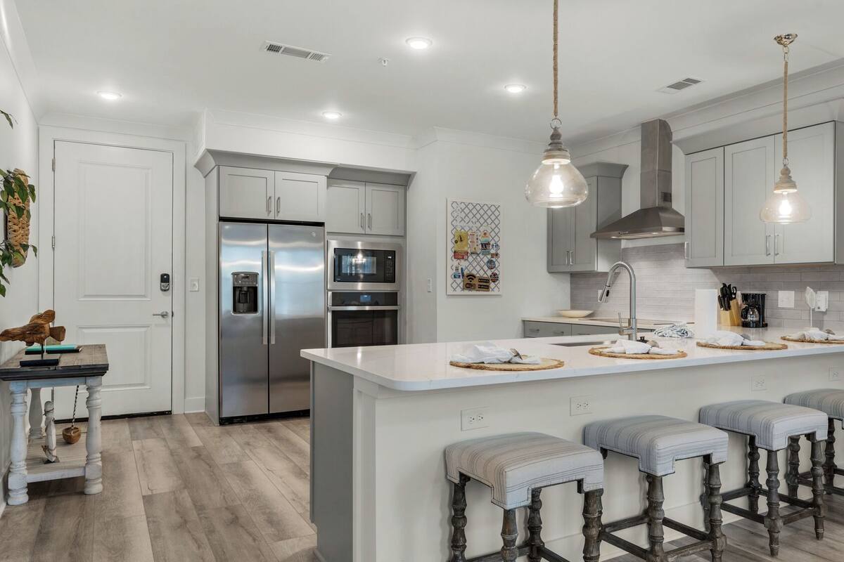 A modern kitchen with stainless steel appliances, a central island with bar stools, and pendant lighting.