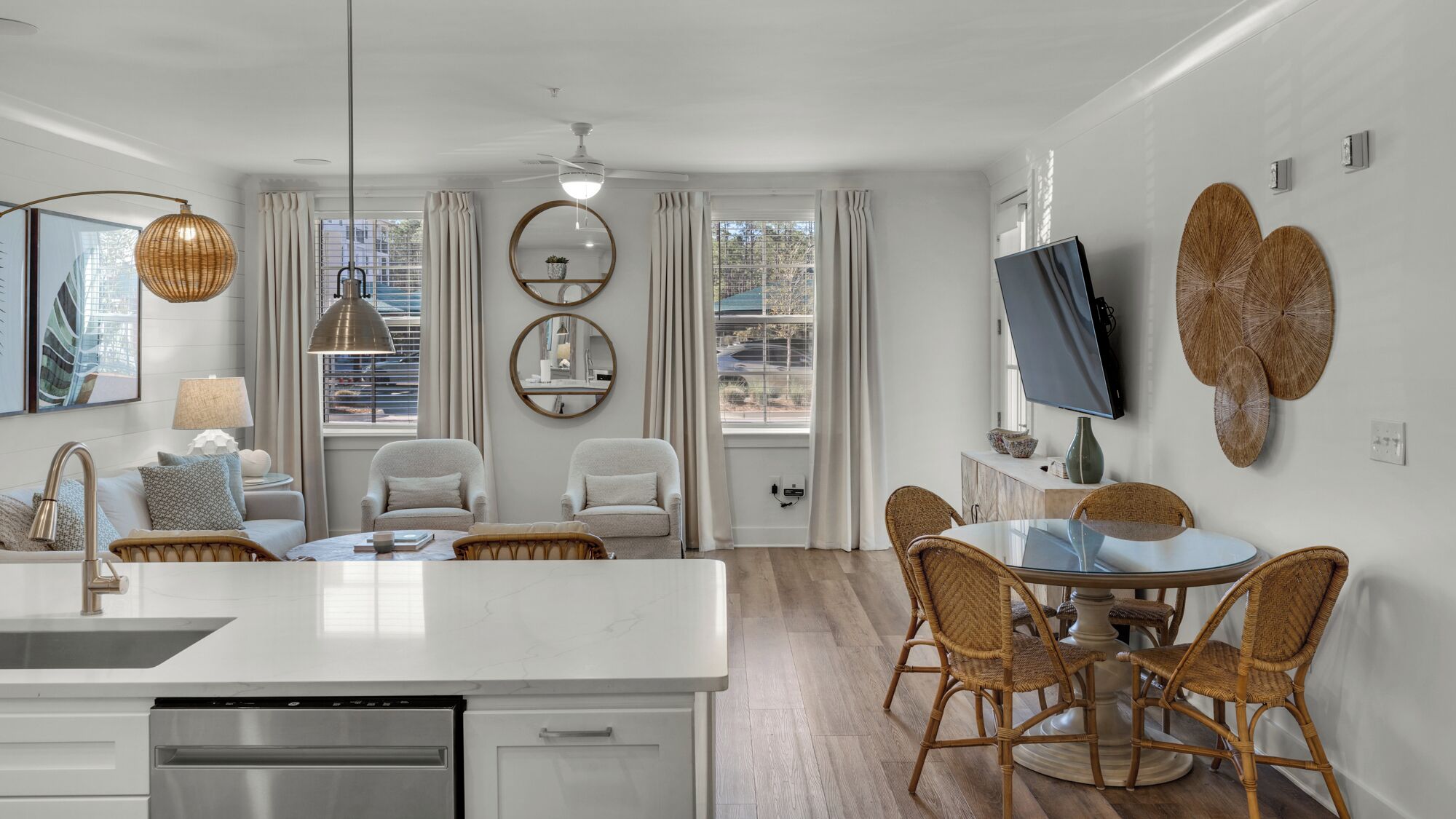 A modern kitchen with a central island, dining area with wicker chairs, and a TV mounted on the wall.