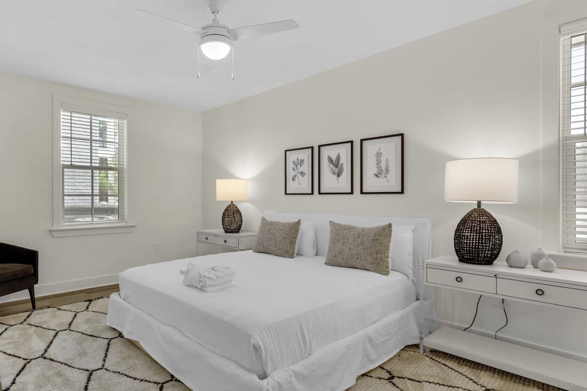 A bedroom with a bed, two bedside tables, a nightstand, a chair, and a ceiling fan.