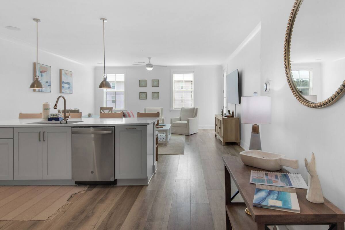 A modern kitchen with a central island, a dining area with a wooden table, and a large mirror on the wall.