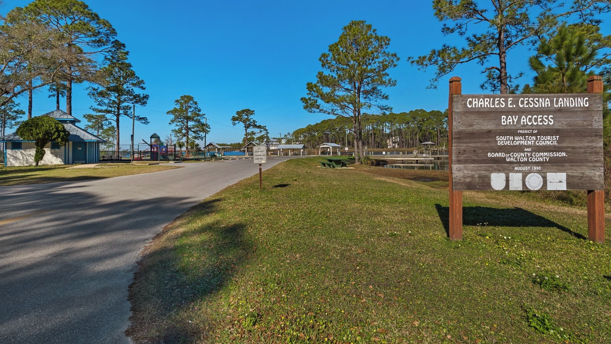 A wooden signboard with text, a road, and a grassy area with trees.