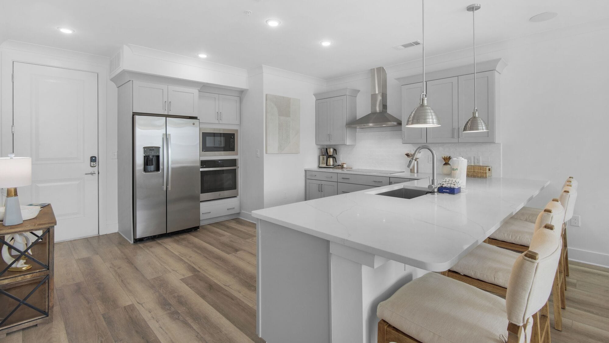 Una cocina moderna con armarios blancos, electrodomésticos de acero inoxidable y una isla central con taburetes de bar.
