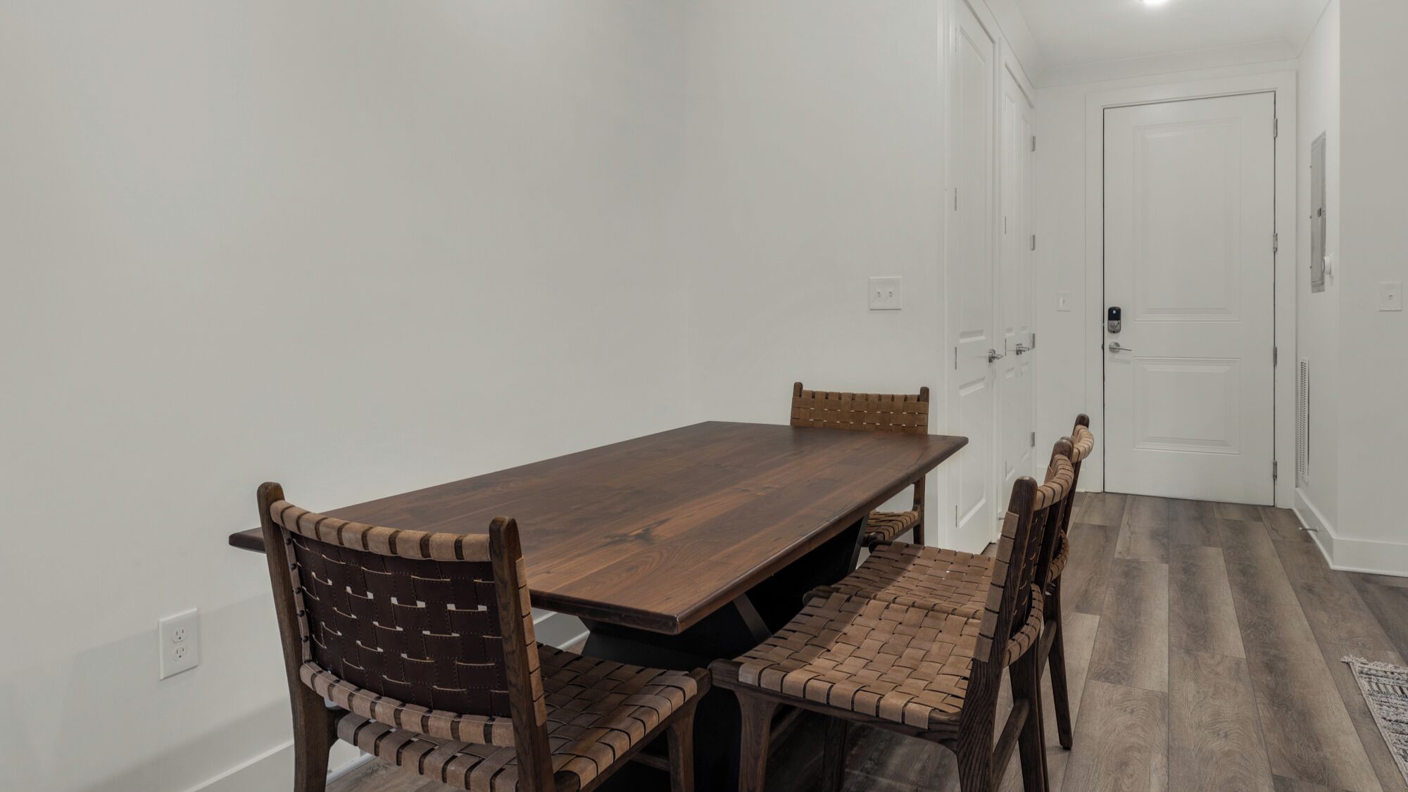 A dining area with a wooden table and chairs, a white door, and a hallway.