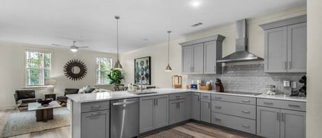 A modern kitchen with grey cabinets, a large island, and a dining area with a sofa and coffee table.