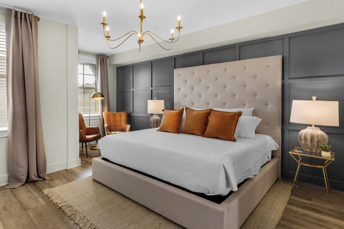 A bedroom with a large bed, two bedside lamps, a chandelier, and a view of the outside through the window.