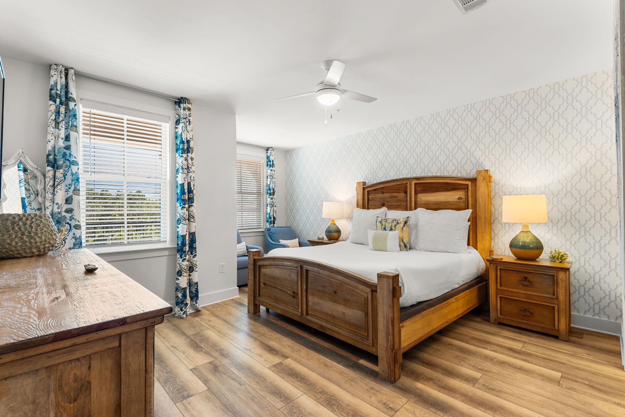 A bedroom with a wooden bed, two bedside tables with lamps, a ceiling fan, and a window with blinds.