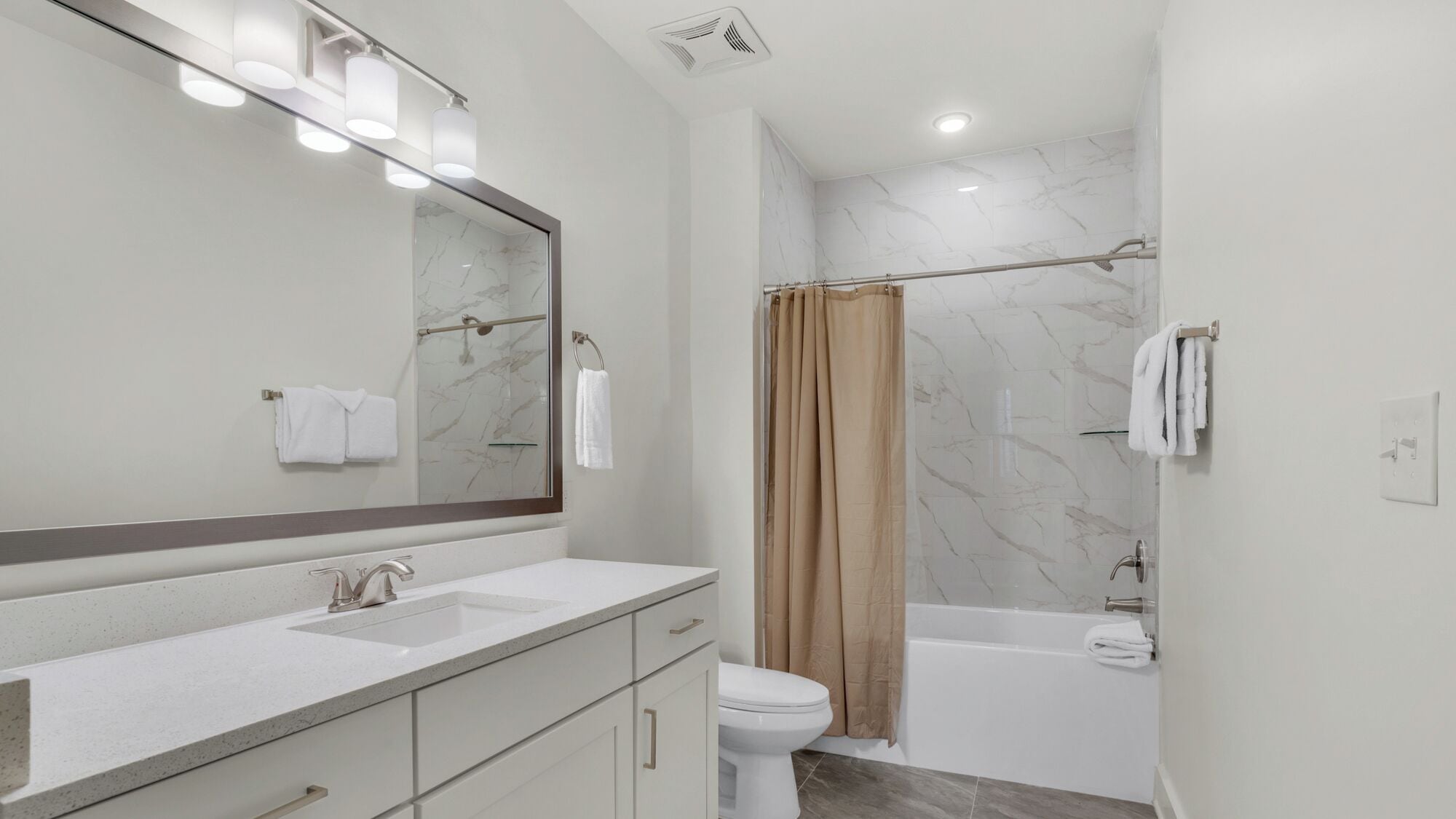 A modern bathroom with a marble shower, a bathtub, and a large mirror with lights.