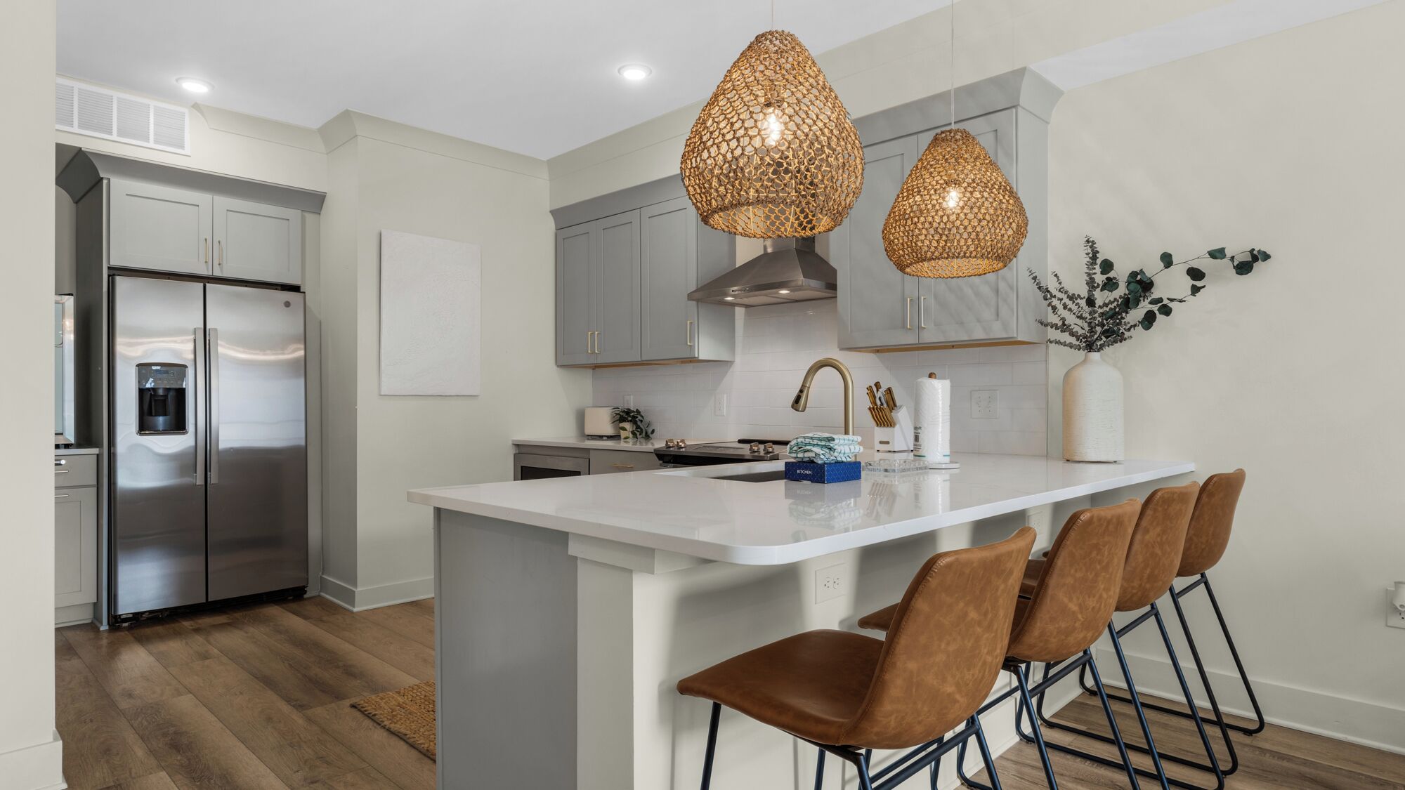 A modern kitchen with a stainless steel refrigerator, a white island with bar stools, and pendant lighting.