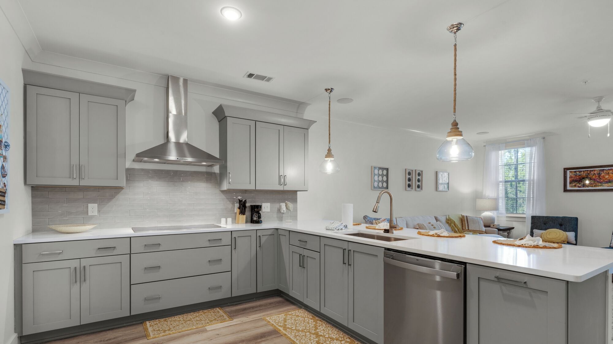 A modern kitchen with grey cabinets, a stainless steel range hood, and a dishwasher.