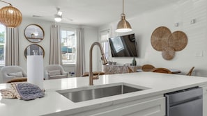 A modern kitchen with a built-in dishwasher, a large island with a sink, and a flat-screen TV mounted above the island.