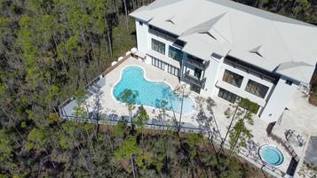 Ett flygbildsfoto av ett modernt hus med en stor swimmingpool, omgivet av ett skogsomrÄde.