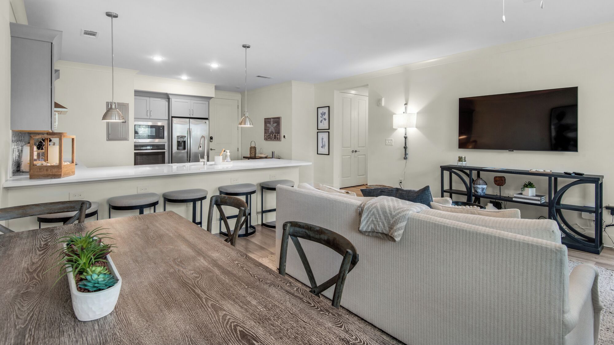 A modern kitchen with a central island, a dining area with a wooden table, and a living room with a sofa and TV.