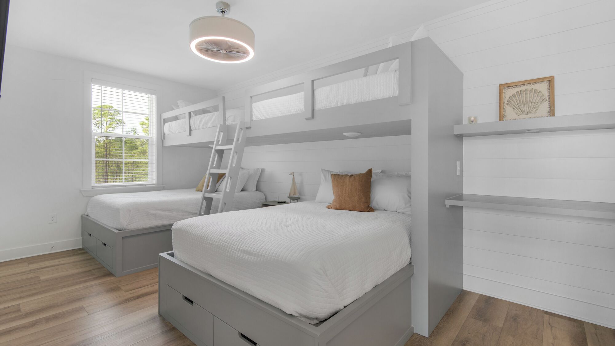 A bedroom with two bunk beds, a ladder, a bedside table, and a window with blinds.