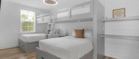 A bedroom with two bunk beds, a ladder, a bedside table, and a window with blinds.