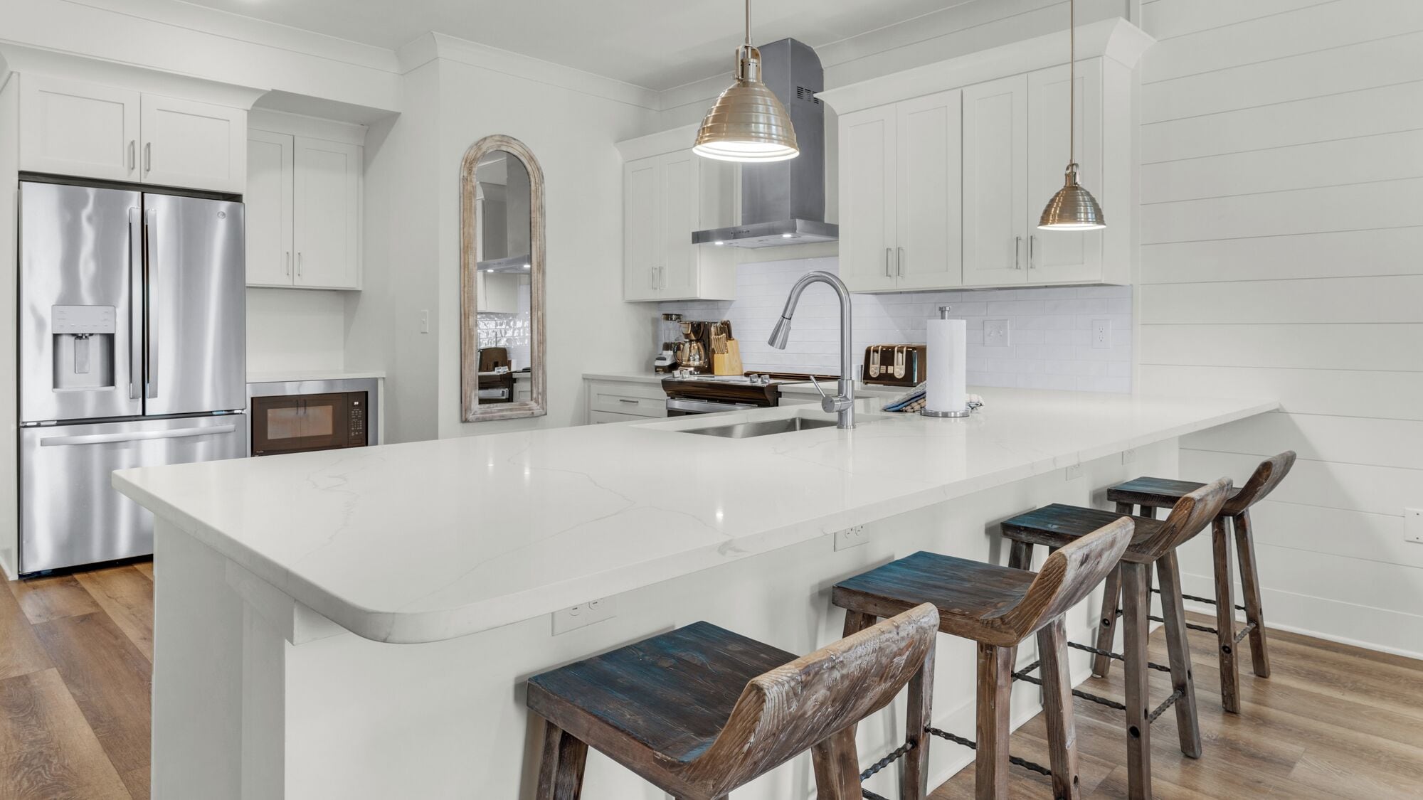 Une cuisine moderne avec des meubles blancs, des appareils en acier inoxydable, un grand îlot central doté de tabourets et un éclairage suspendu.
