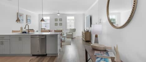 A modern kitchen with a central island, a dining area with a wooden table, and a large mirror on the wall.