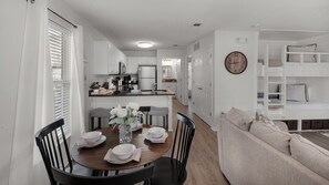 A modern kitchen with white cabinets, a central island, and a dining area with a wooden table and chairs. - Rollin Tide Villas (Santa Rosa Beach)