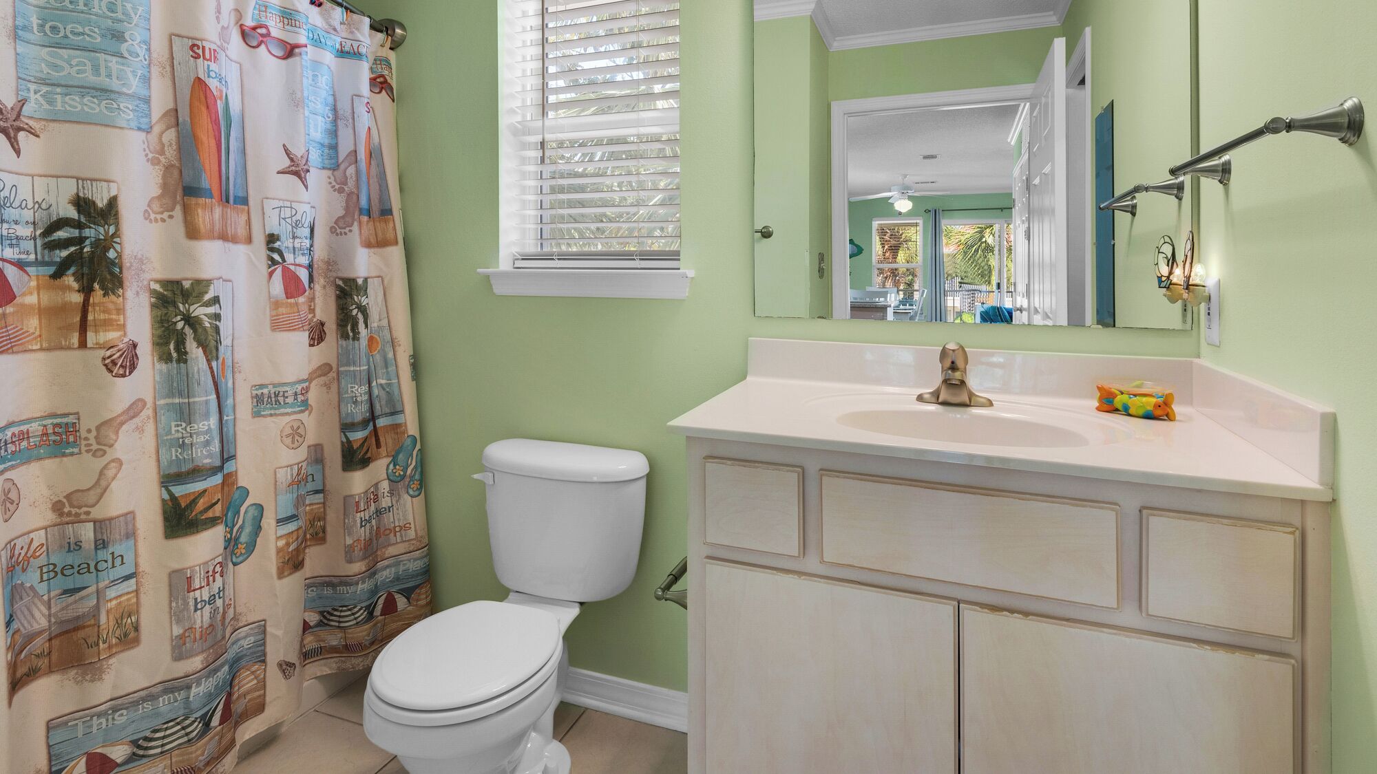 A bathroom with a white toilet, a sink with a gold faucet, and a shower curtain with beach-themed designs.