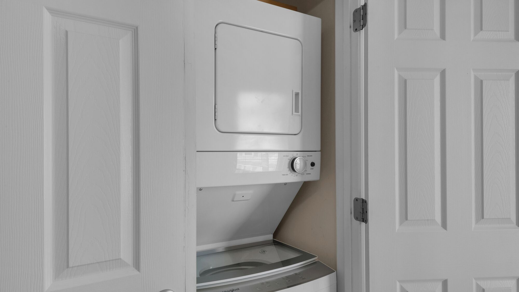 A white laundry room with a front-loading washer and dryer, a control panel, and a small shelf.