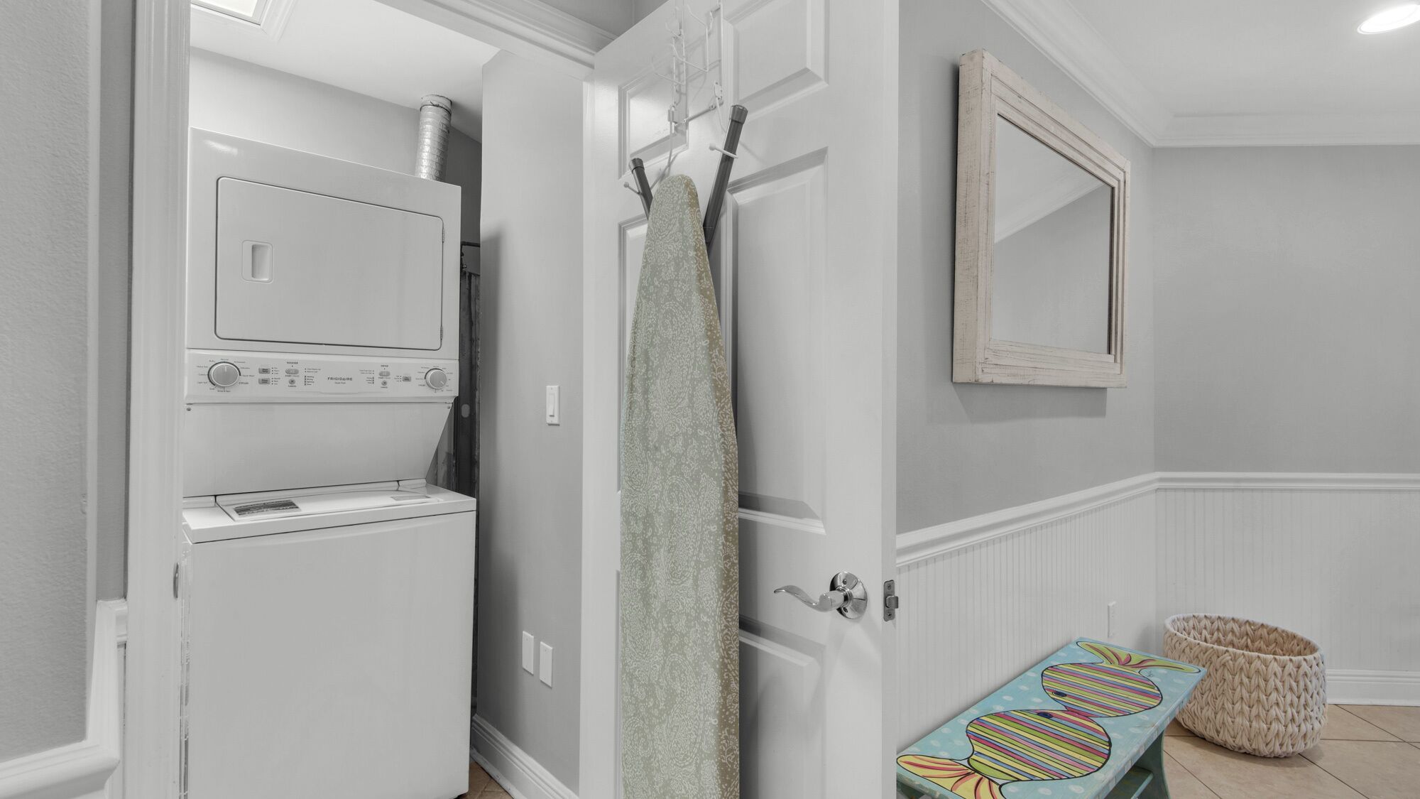 Une buanderie équipée d’un lave-linge et d’un sèche-linge à chargement frontal, d’un porte-serviettes, d’un miroir et d’un tapis coloré sur le sol.