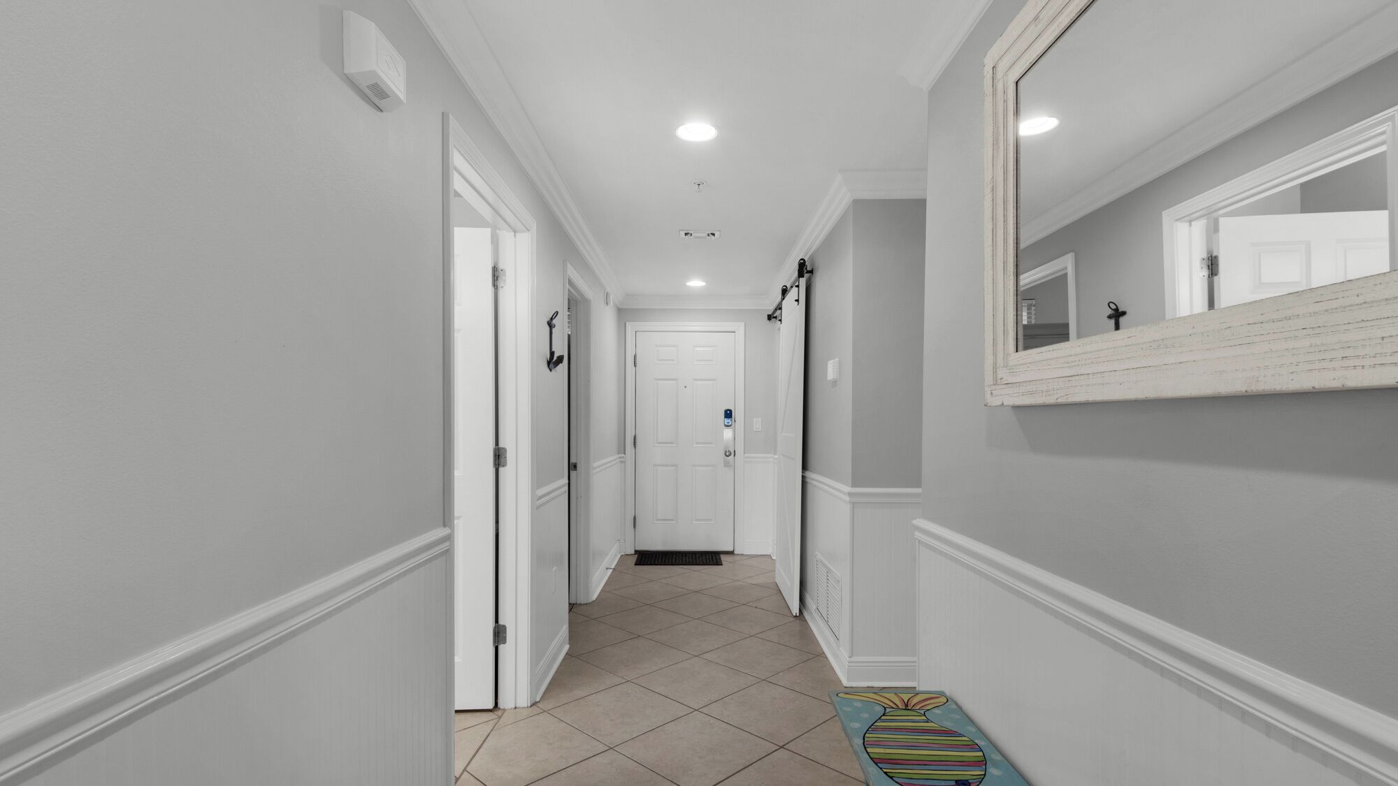 A narrow hallway with white walls, a tiled floor, and a door at the end.