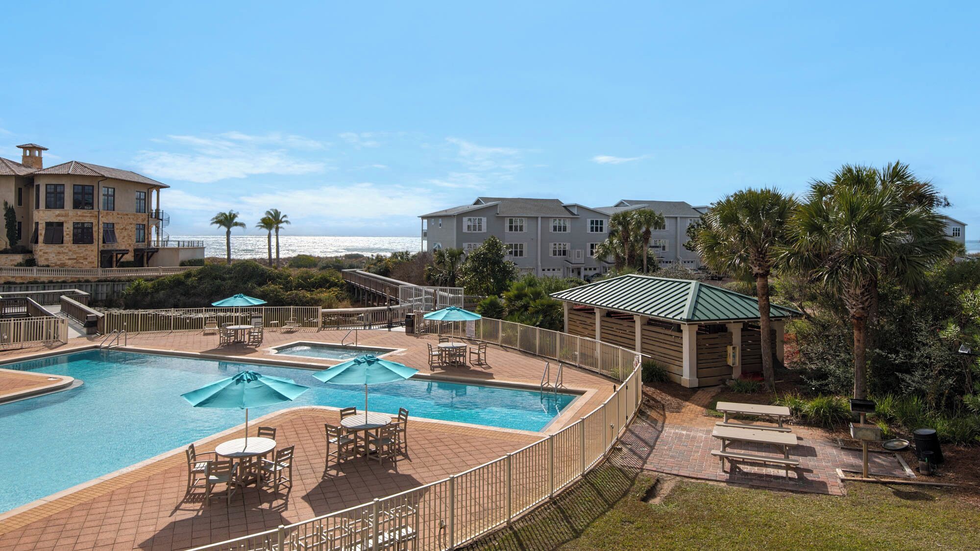 A swimming pool with lounge chairs and umbrellas, surrounded by a fence and a view of the ocean.