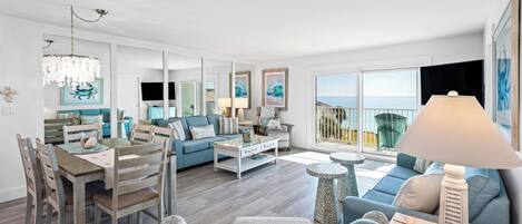Amplia sala de estar con comedor, un balcón con vista al mar y un ventanal grande.