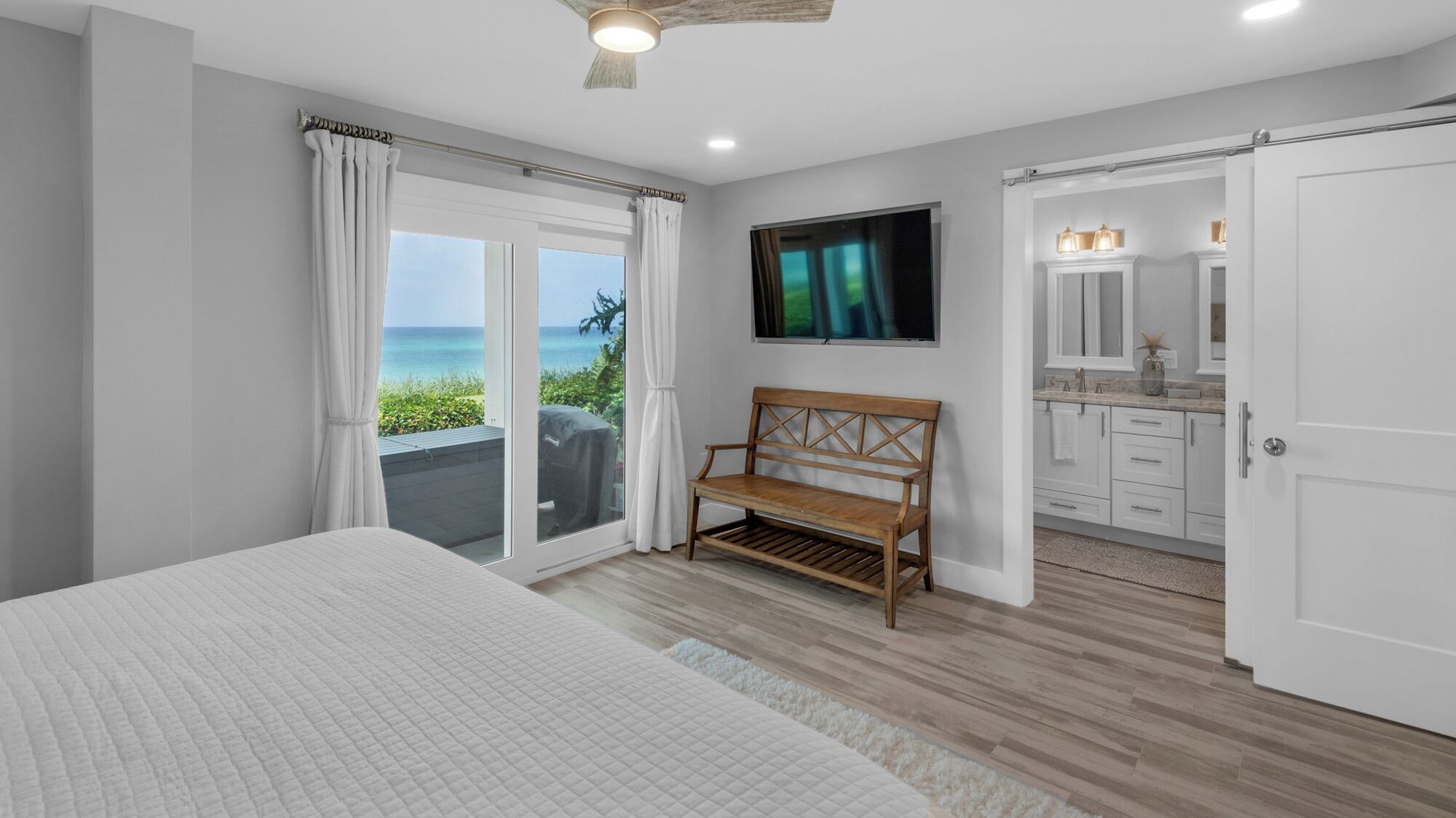 A bedroom with a large bed, a bench, a TV, and a view of the ocean.
