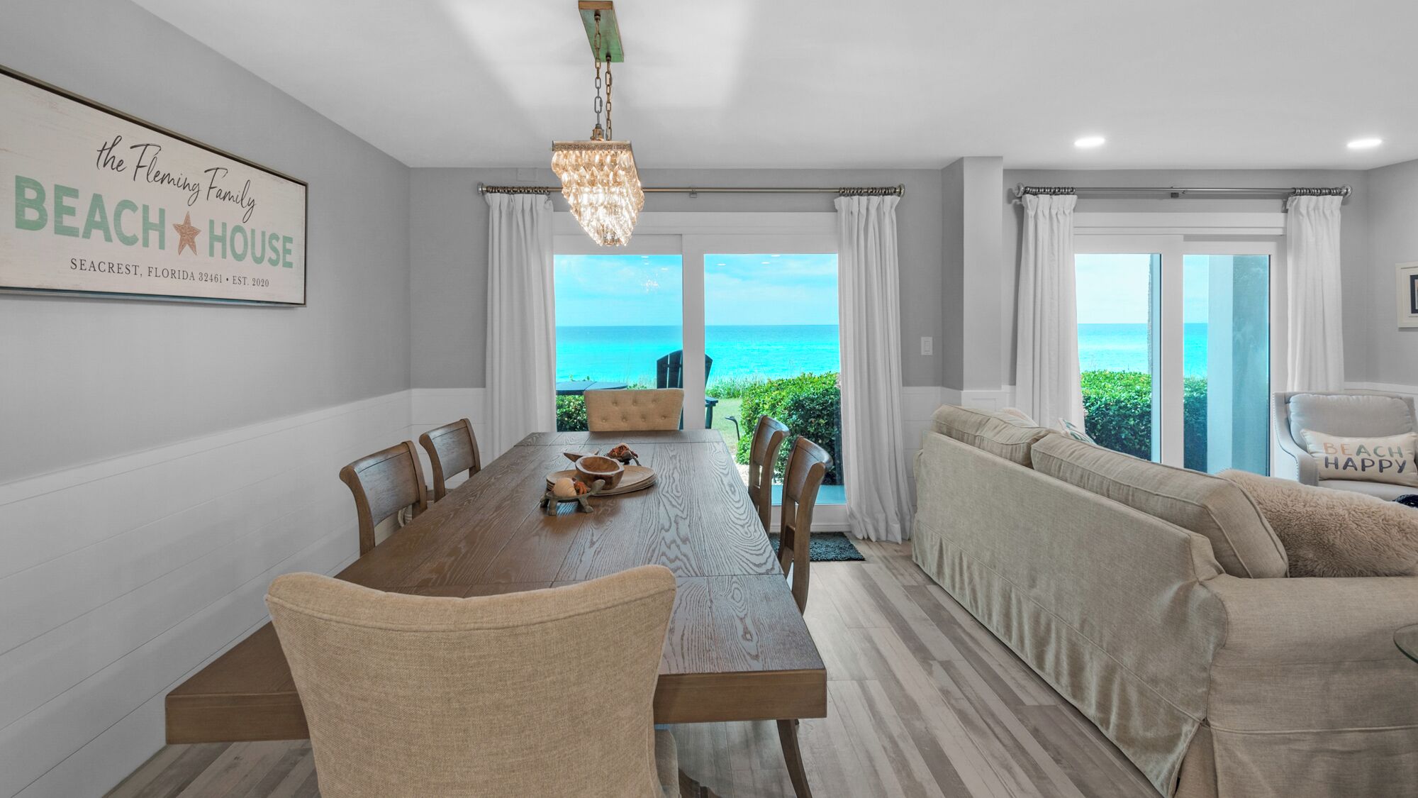 Un espace repas offrant une vue sur l’océan, une enseigne sur le thème de la plage et un coin salon confortable.