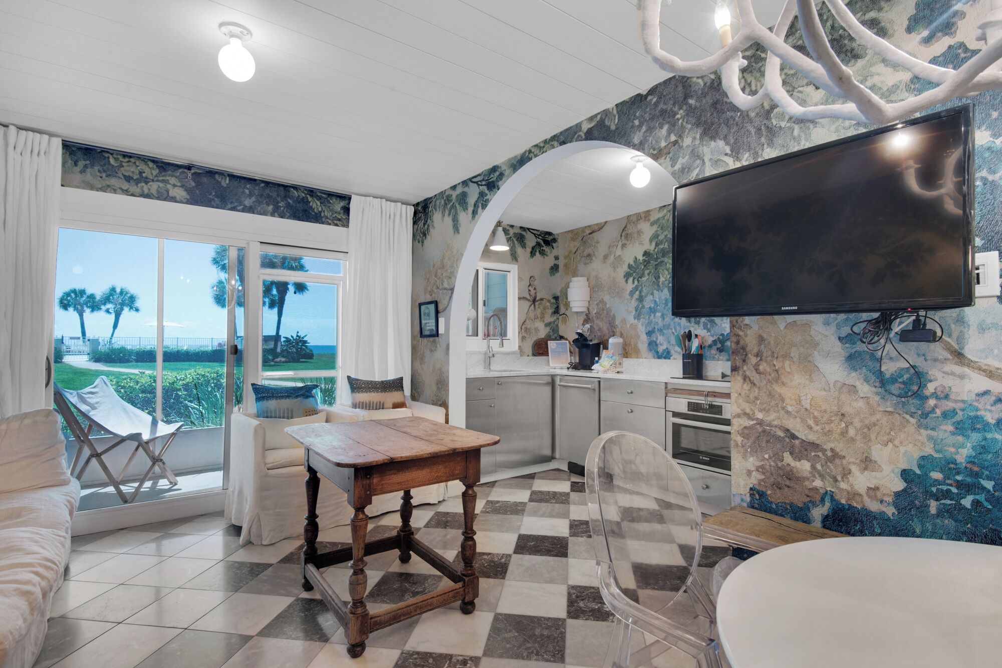 A modern living room with a large TV, a dining table, and a view of the outdoors.
