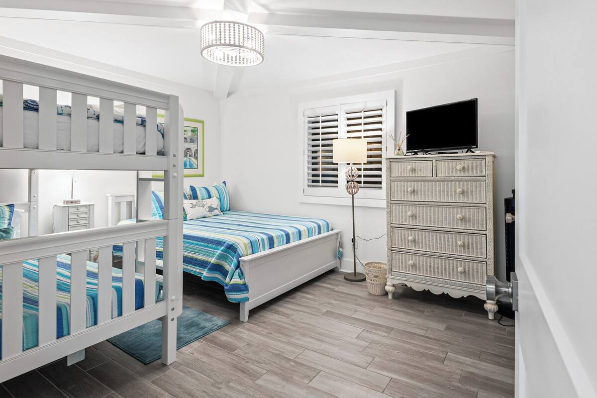 A bedroom with bunk beds, a single bed, a dresser, a lamp, and a television.