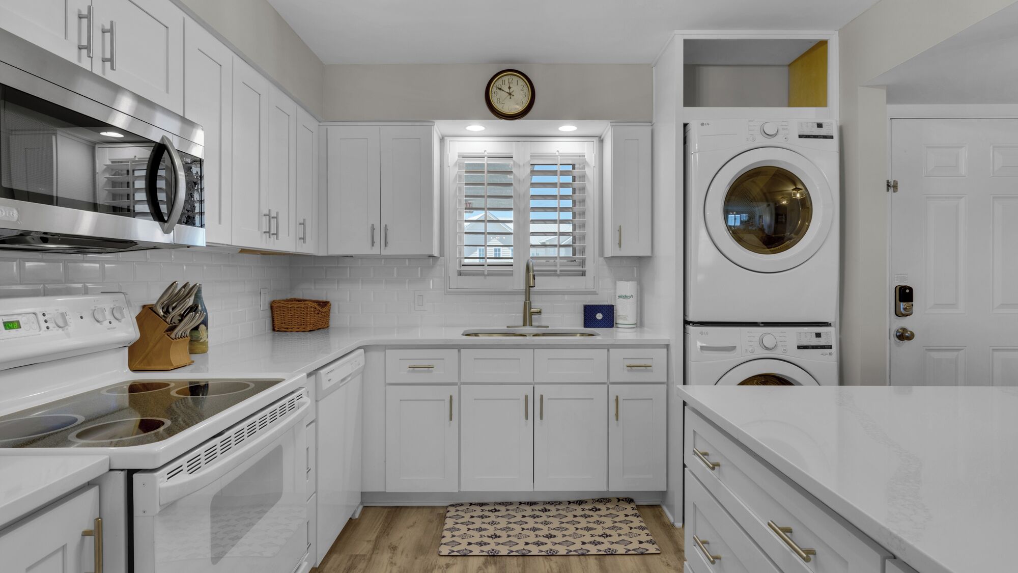 A modern kitchen with white cabinets, a stainless steel range, a built-in oven, a microwave, a sink with a gold faucet, and a built-in washer and dryer.