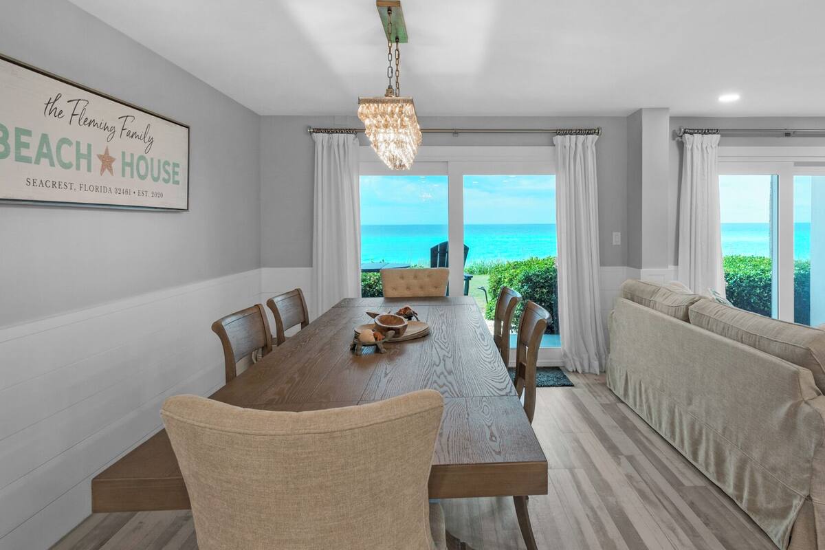 Un espace repas offrant une vue sur l’océan, une enseigne sur le thème de la plage et un coin salon confortable.