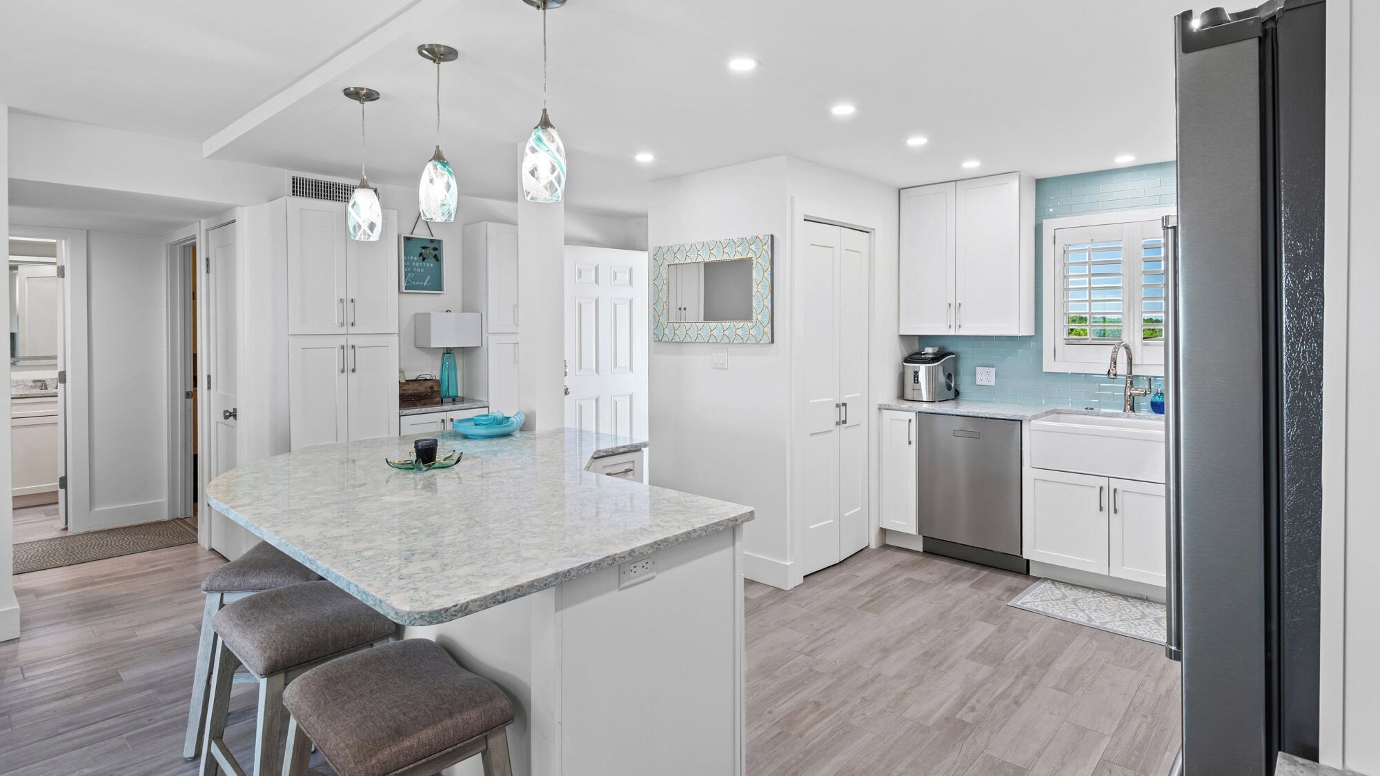 A modern kitchen with white cabinetry, a marble island, and pendant lighting.