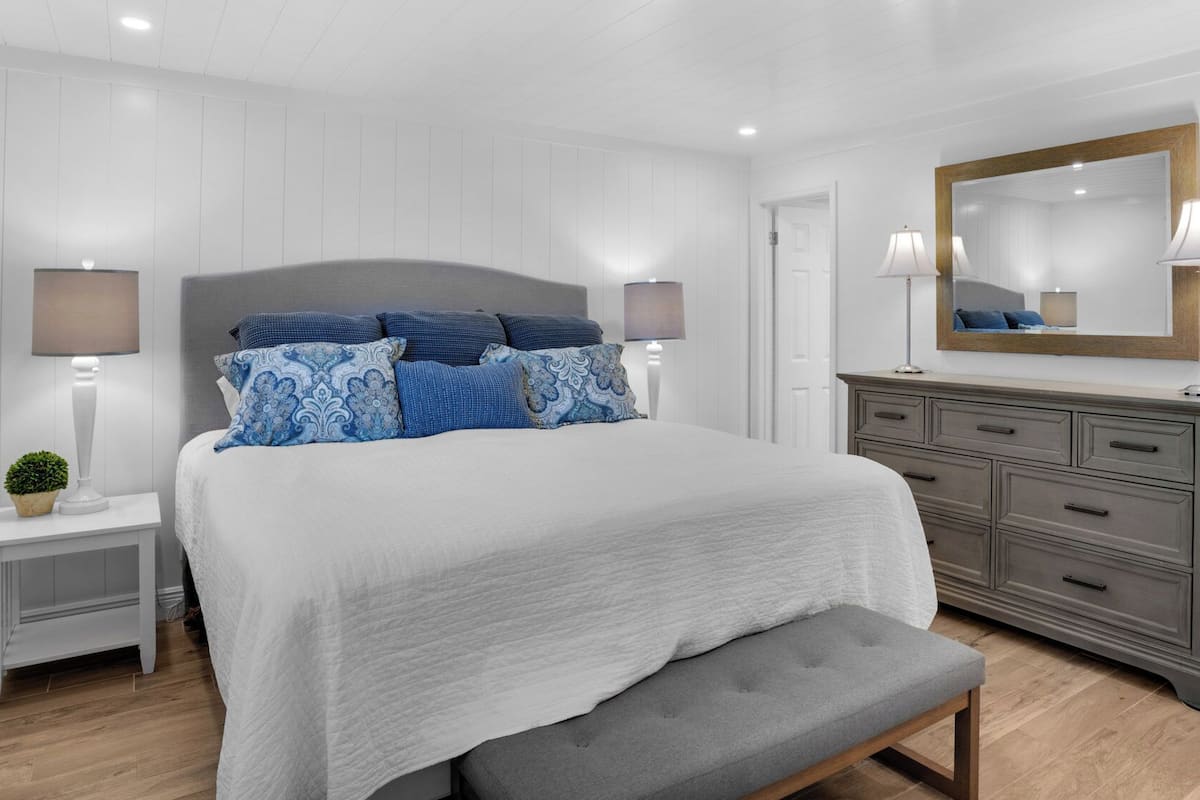 A bedroom with a bed, bedside tables, a dresser, a bench, and a mirror.