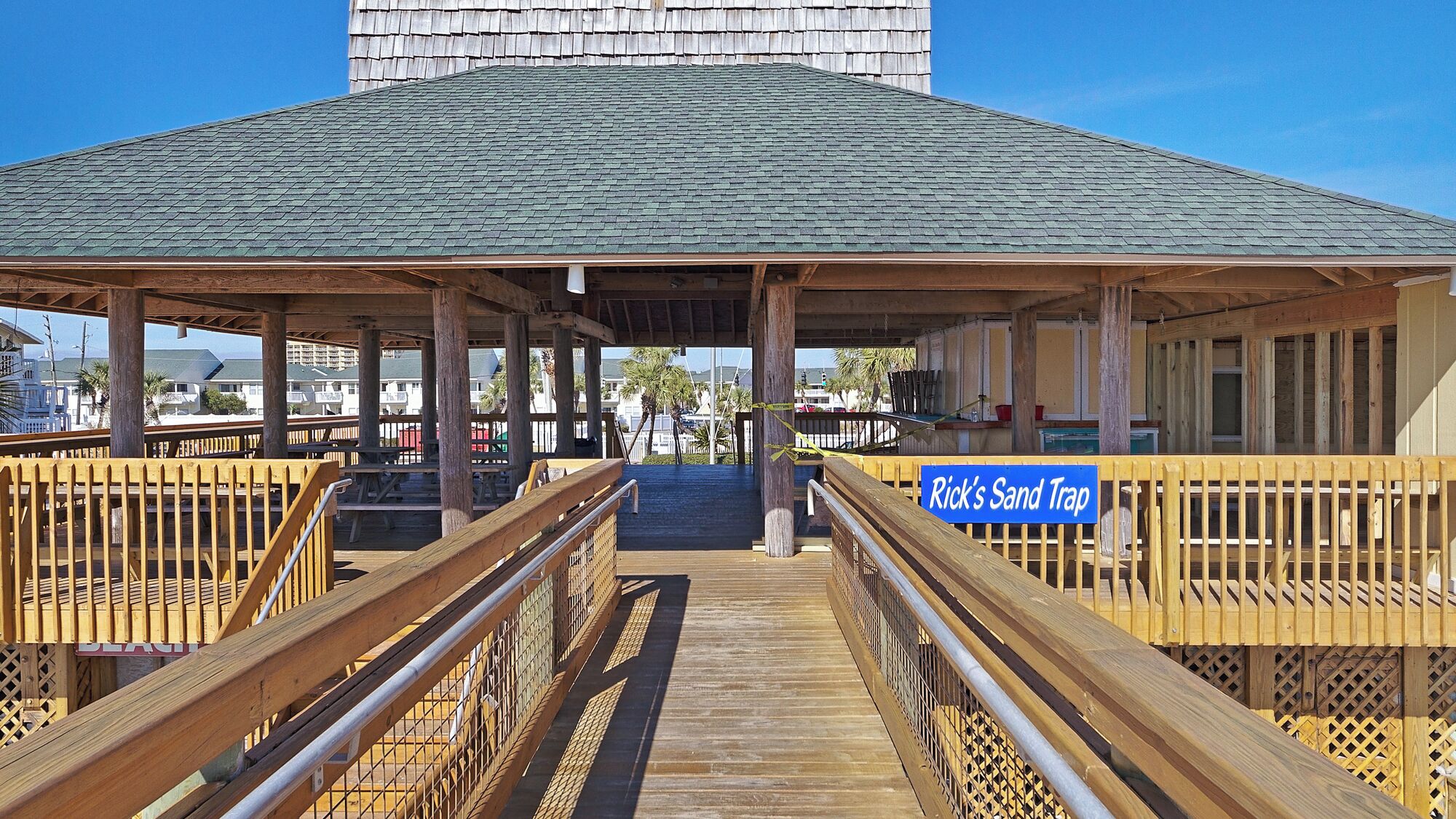 A wooden boardwalk leading to a covered area with a sign reading "Rick's Sand Trap".