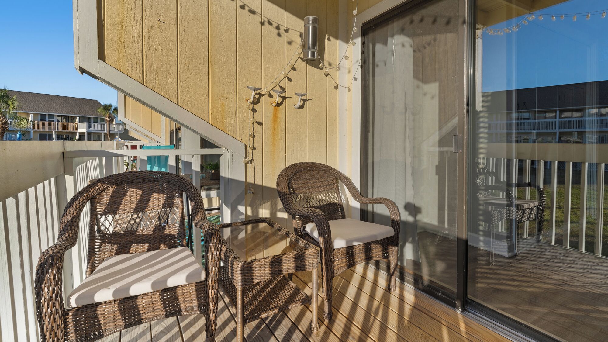 Un balcon avec des fauteuils en osier et une table, une porte vitrée et une guirlande lumineuse.