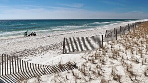 A beach with a wooden fence and a sandy area with sparse vegetation. - Sandpiper Cove (Destin)