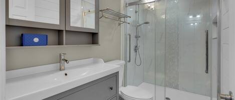 A modern bathroom with a white sink, a toilet, and a glass-enclosed shower area.