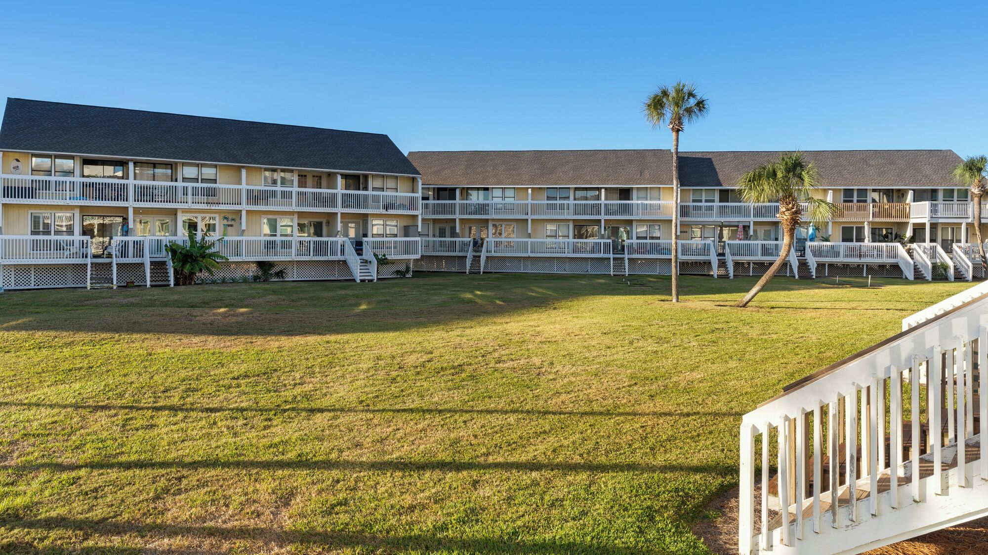 A multi-story hotel with a flat roof, white railings, and a grassy lawn.