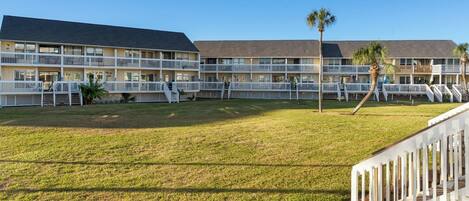 A multi-story hotel with a flat roof, white railings, and a grassy lawn.