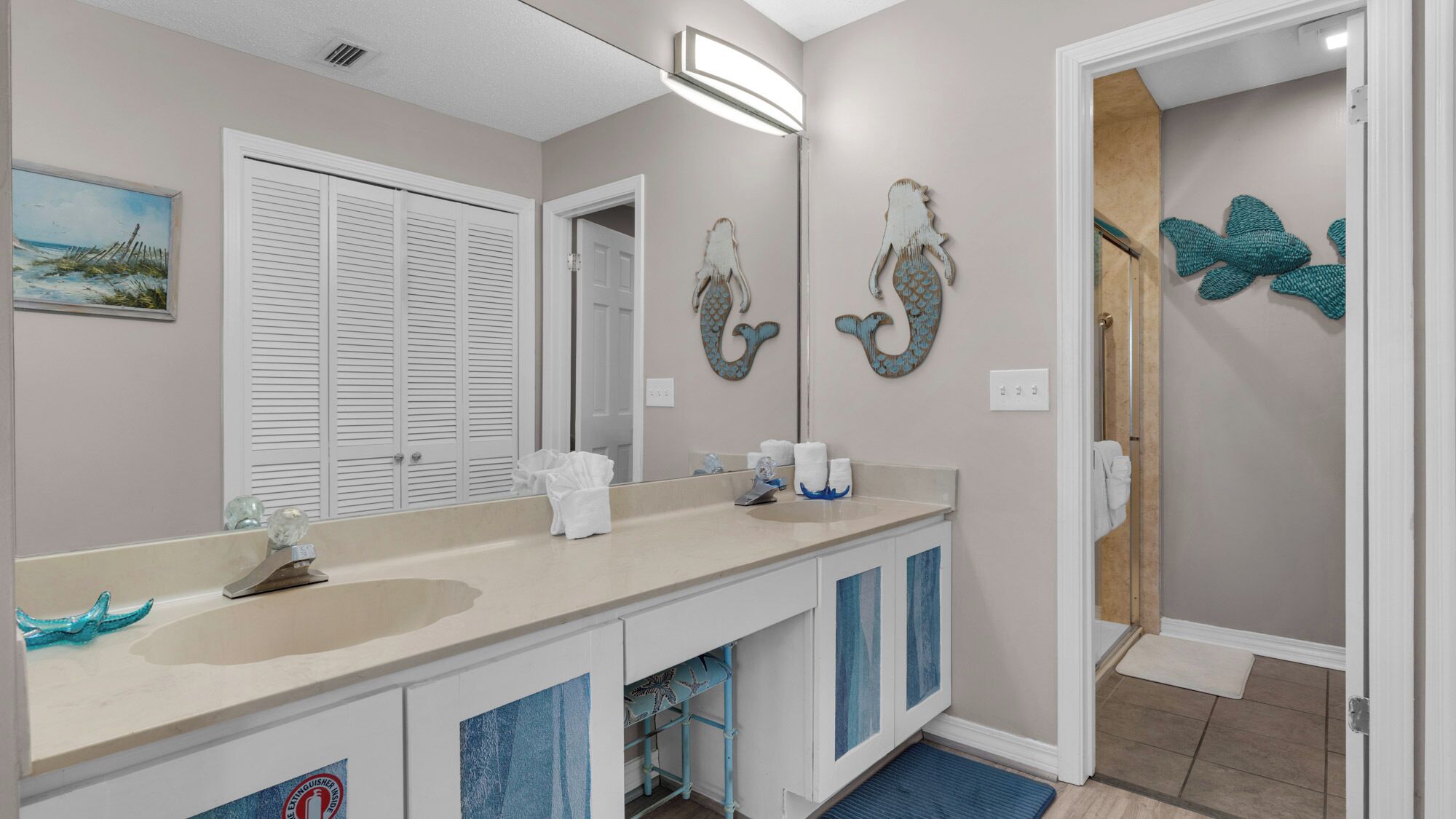 A bathroom with a double sink, a mirror, and decorative wall art.